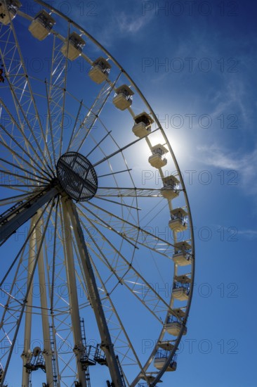 Bright sun shines behind a towering Ferris wheel, creating a vibrant atmosphere at an amusement