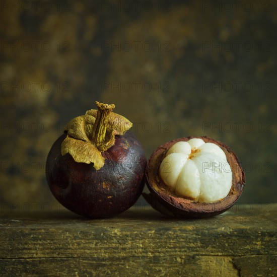 Two ripe mangosteens rest side by side, showcasing their deep purple skin. One fruit is cut in