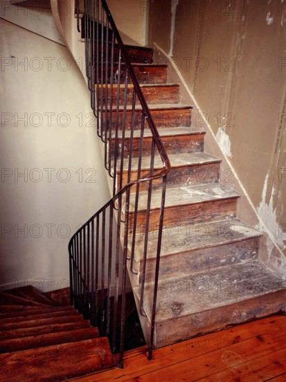 A winding staircase constructed from rustic wood features elegant iron railings, set in a partially