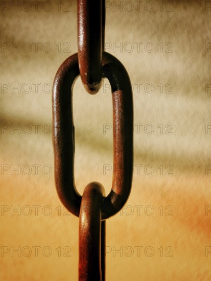 Close-up of a rusty chain with interlocking links suspended against a softly blurred warm backdrop.
