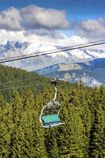 A ski lift transports visitors above green forests toward snowy mountain peaks in Haute-Savoie,