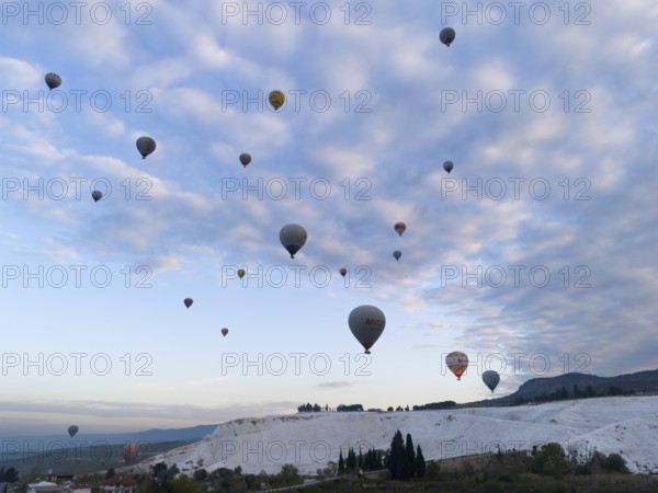 Hot air balloons float over a picturesque landscape under a cloudy sky, aerial view, Pamukkale,