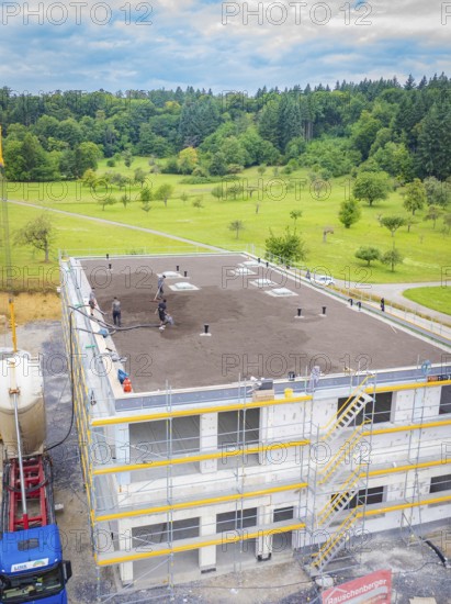 Partly completed building with workers in a landscaped environment, surrounded by forest, green