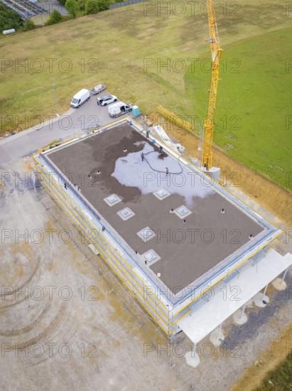 Building in shell construction with crane and vehicles on an open plot with surrounding fields,