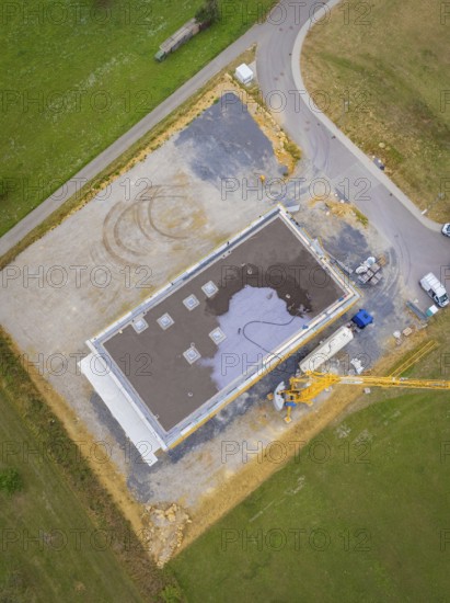 Aerial view of a rectangular building in shell construction on a large site next to a road, green