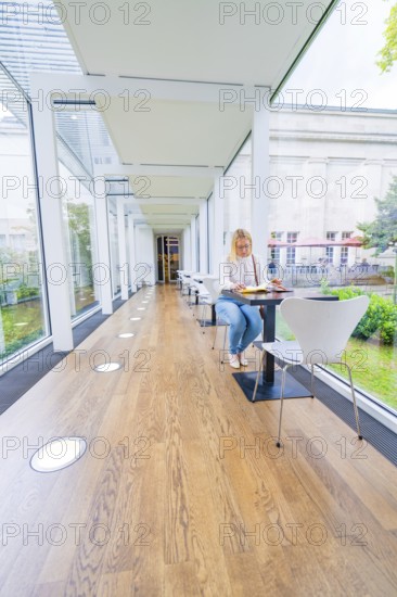 Woman sitting at a table in a light-flooded café with large glass walls, Frieder Burda Museum,