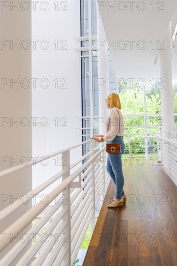 A woman stands at a railing and looks through a large window at the surroundings, Frieder Burda