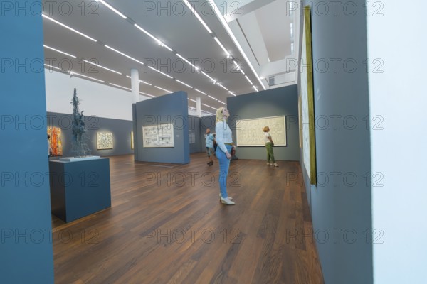 People looking at paintings in a modern art gallery with wooden floor and dark walls, Frieder Burda