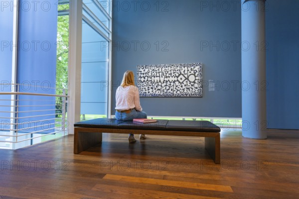 A woman sits on a bench in front of a modern work of art and looks at it attentively, Frieder Burda