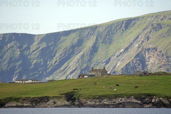 A remote house stands in green pasture against a dramatic mountain backdrop, Sumburgh, Shetland