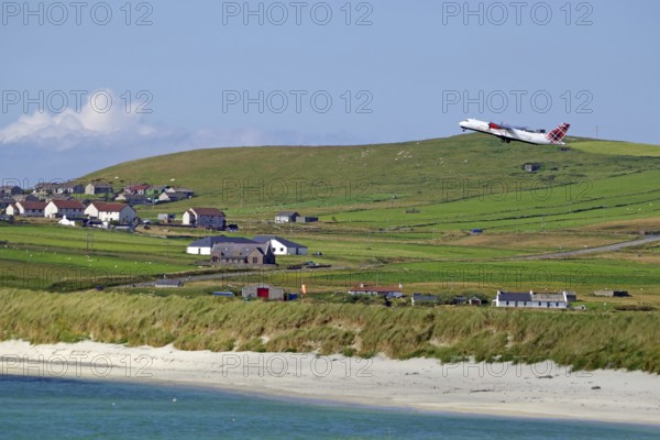 An aeroplane takes off over wide meadows and a coastal village with sea views, Sumburgh Head,