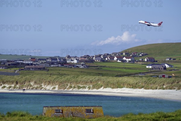 An aeroplane takes off near a rural village with beach and meadows, Sumburgh Head, Shetland
