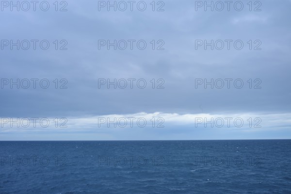 A calm sea stretches to the horizon with thick clouds in the sky, summer, Cook Strait, North