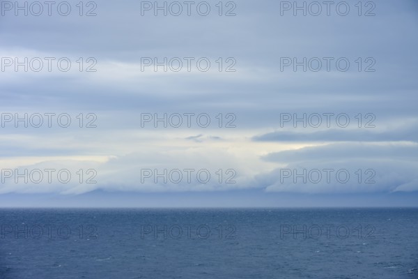 Calm sea under a dense canopy of clouds, mountains visible in the distance, summer, Cook Strait,