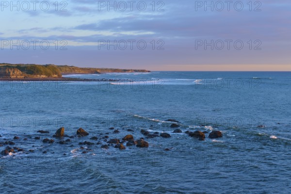 Rocks in the sea under a pink-orange sky at sunset, summer, Opunake, Taranaki, North Island, New