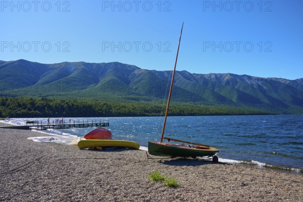 Boats moored on the shore of a lake with a breathtaking mountain backdrop and clear blue sky,