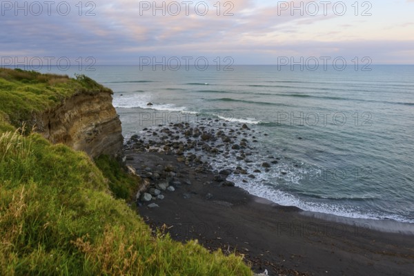 Seaside cliff with rocks and green vegetation under a cloudy sky, summer, Opunake, Taranaki, North