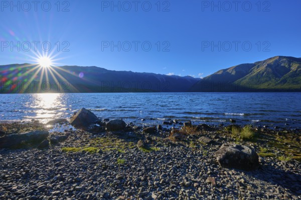 Sunlight dazzles over the horizon as it hits the tranquil lake and surrounding mountains, summer,