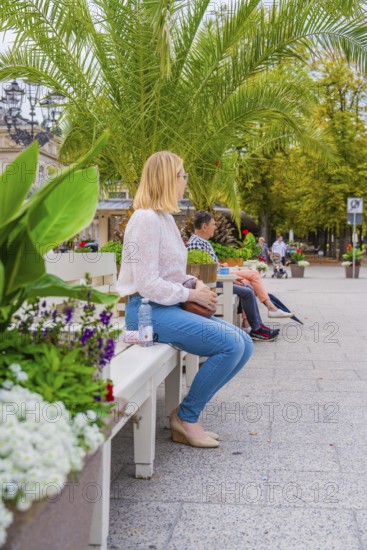 People sitting on a park bench surrounded by green plants and trees in the city, Baden Baden,