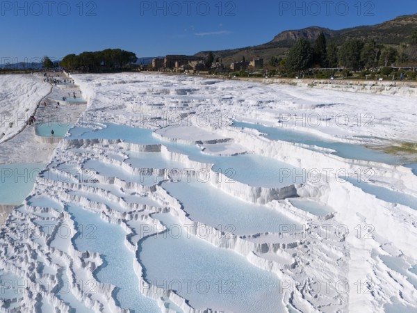 Extensive limestone sinter terraces with water and surrounding landscape in Pamukkale, aerial view,