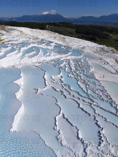 Terraces of turquoise water in white formations, mountains visible in the background under a clear