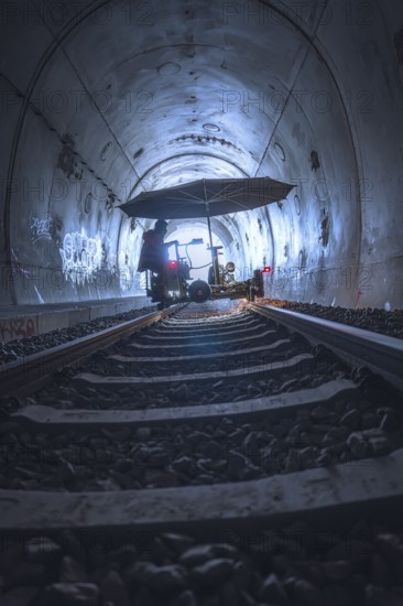 A mysterious tunnel with rails and graffiti, illuminated by a diffuse light. A figure stands under