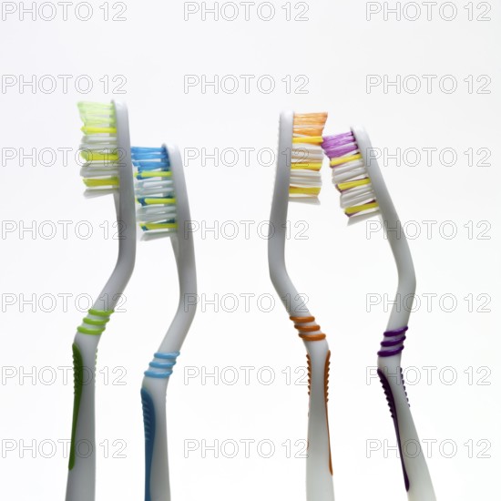 Four vibrant toothbrushes in varied colors stand side by side against a simple background,