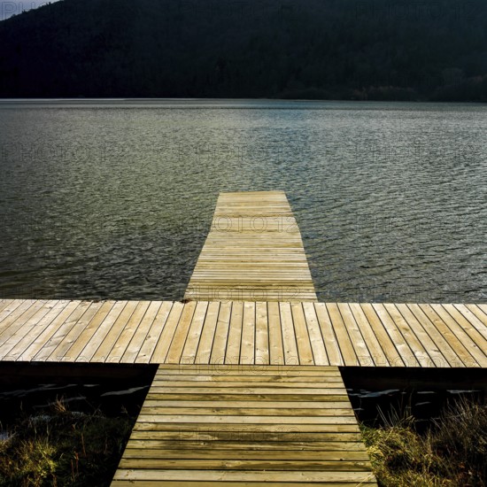 A wooden dock reaches out over serene waters reflecting nearby hills, providing a peaceful spot for
