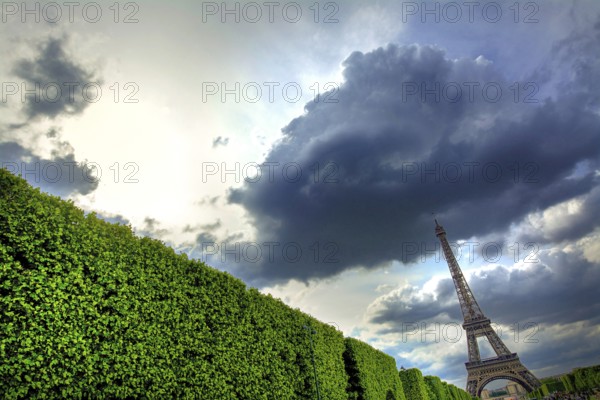 Clouds blanket the sky above the Eiffel Tower, creating a striking contrast with the greenery below