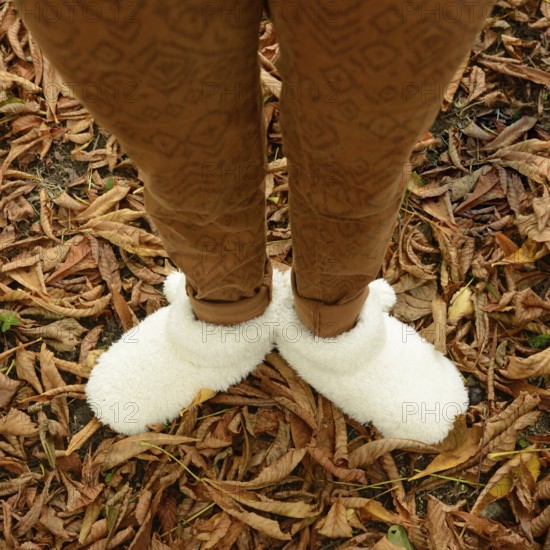 A young woman stands among fallen leaves, wearing warm, fluffy shoes that provide comfort. The