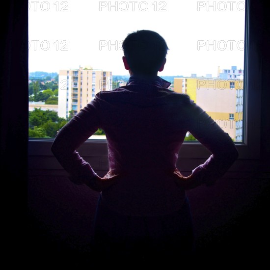 A woman stands by a window, hands on her hips, looking out at the cityscape of France. The bright