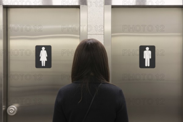 Woman in front of men's and women's bathroom doors. Concept of public restroom access and trans