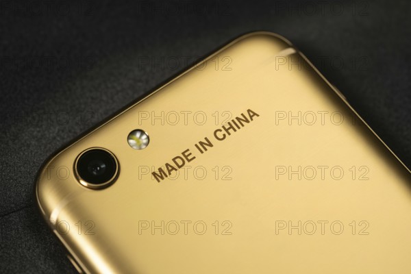 Close-up of engraved Made in China text on the back of a shiny golden smartphone. Concept of