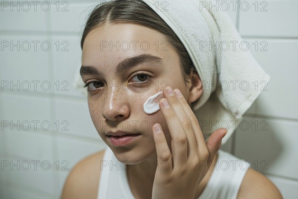 Teenage girl applying skin cream in bathroom. Honest daily skincare and self-care routine.