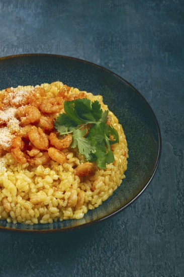 Risotto with shrimp, in a bowl, on a textured surface, with a side dish of fresh coriander,