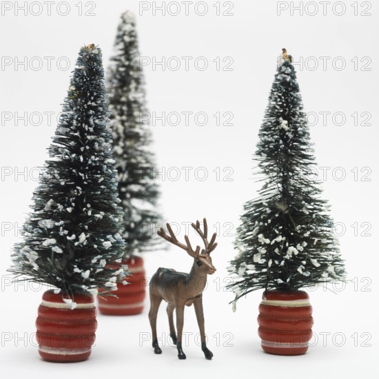 A detailed deer figurine stands in front of two snowy miniature trees, creating a festive