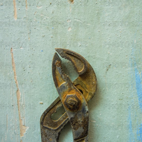 A pair of rusty pliers hangs on a worn blue wall, showcasing the wear and tear of years in a