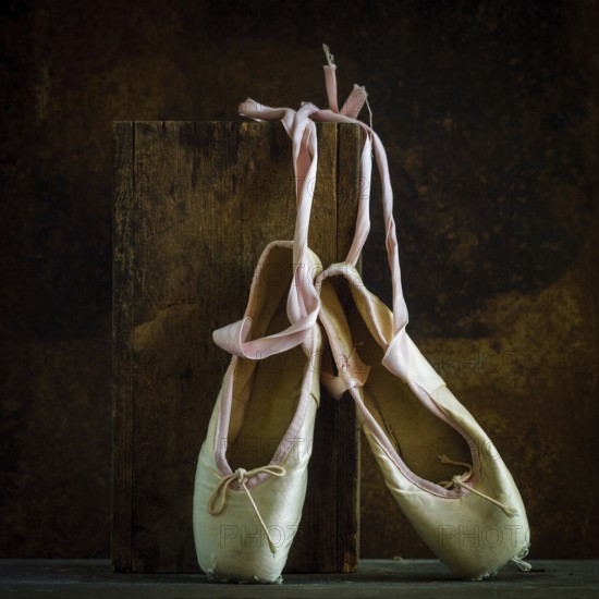 Delicate ballet shoes are placed on a wooden block, showcasing their soft texture and ribbons. The
