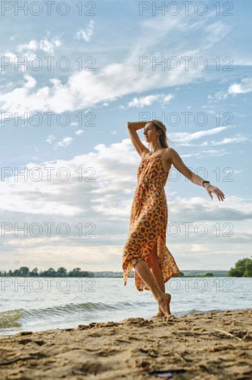A woman stands barefoot on sandy shores, wearing a bright dress with a bold floral pattern. She