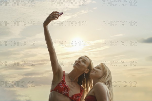 Two friends capture a joyful moment taking a selfie with the sun setting behind them. Dressed in