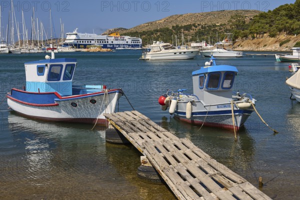 Two small boats on a jetty with a large ferry and yachts in the background, Lakki, Leros,