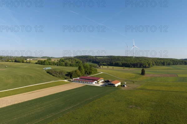 An expansive field landscape with a farm and wind turbines, under a clear blue sky, near