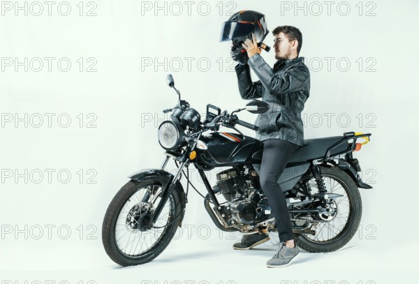 Man on motorcycle putting on helmet, isolated background. Young motorcyclist wearing safety helmet.