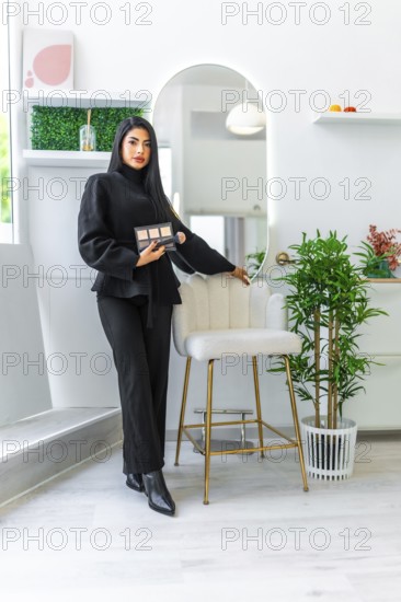 Beautician posing with makeup palette in modern beauty salon, showcasing her expertise and the