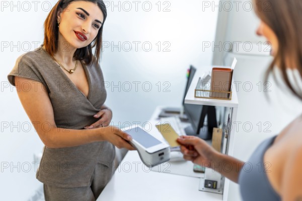 Beautician holding a pos terminal accepting contactless payment from a female customer with a