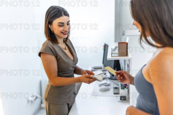 Smiling beautician holding pos terminal while female customer making contactless payment with