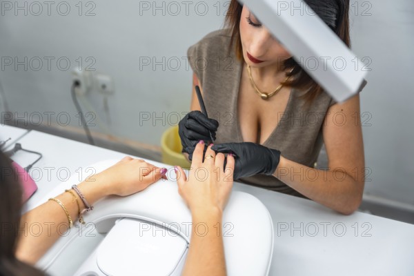 Beautician wearing black gloves carefully applying nail polish on client's hand, providing