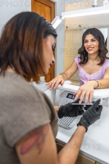Beautician wearing black gloves attentively filing the nails of a smiling customer in a modern