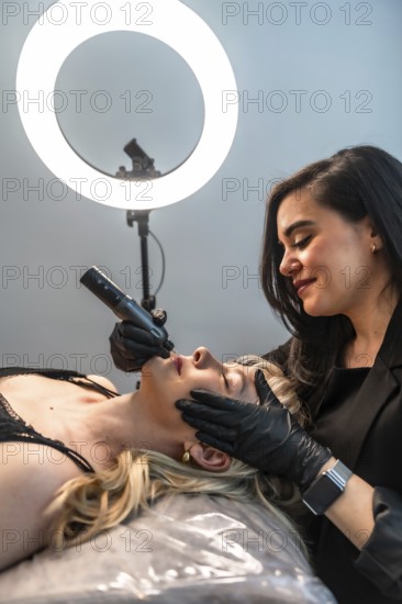 Beautician performing a lip blushing treatment using a rotary tattoo pen in a modern aesthetic