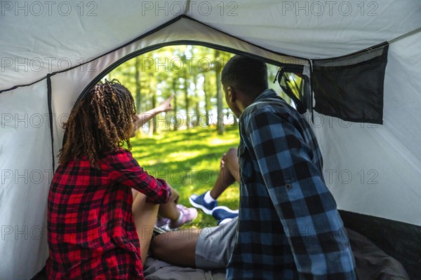 Two tourists sitting inside their tent, excitedly pointing at something intriguing in the lush
